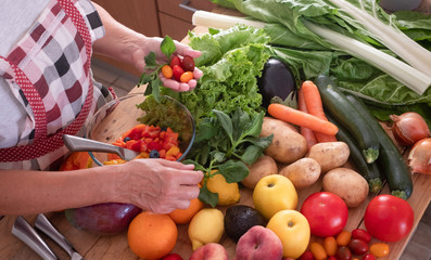 Above view of two hands of a senior woman working to do a fresh fruit salad. Wooden table with a large group of colorful fruits and vegetables. Healthy eating