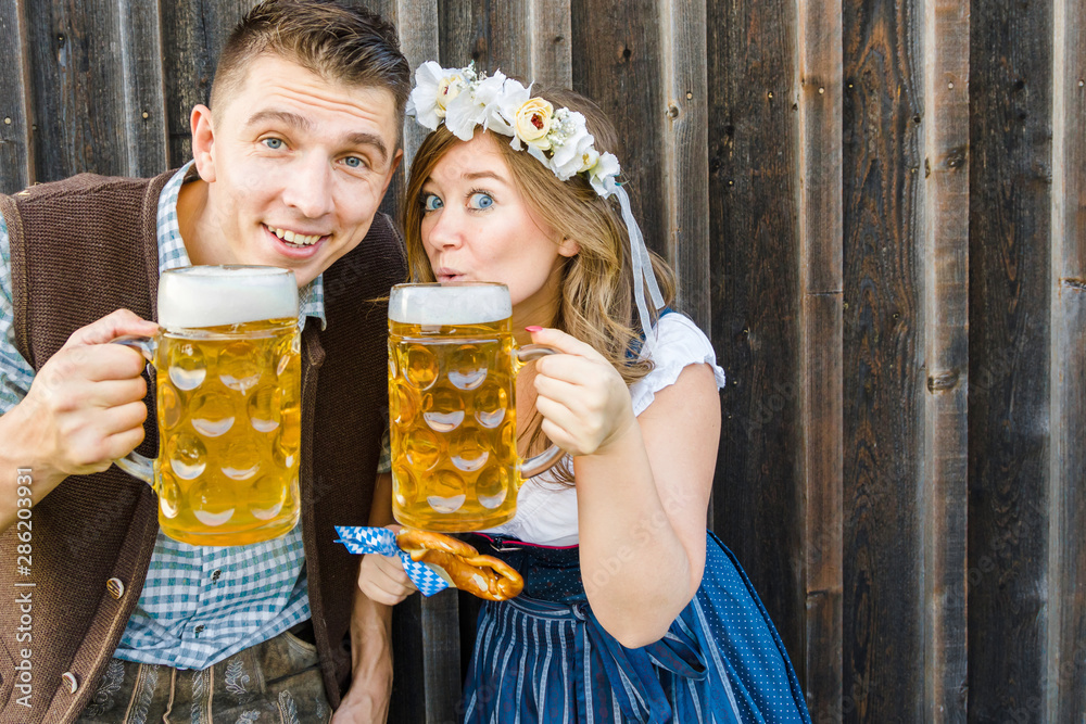 Wall mural Junge Frau und mann mit Bierkrug und Brezel auf einem Holzhintergrund .Oktoberfest-Konzept 