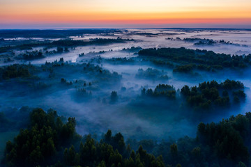 Fototapeta premium Aerial view of the forest, field and river covered with layers of thick morning fog