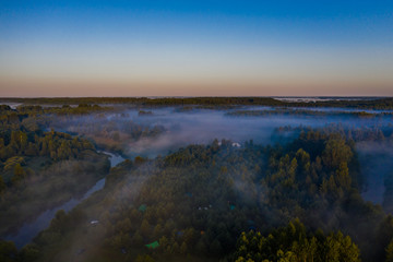 Fototapeta na wymiar Aerial view of the forest, field and river covered with layers of thick morning fog