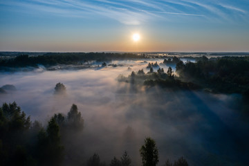 Aerial view of the forest, field and river covered with layers of thick morning fog