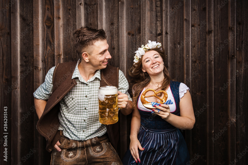 Wall mural Junge Frau und mann mit Bierkrug und Brezel auf einem Holzhintergrund .Oktoberfest-Konzept 