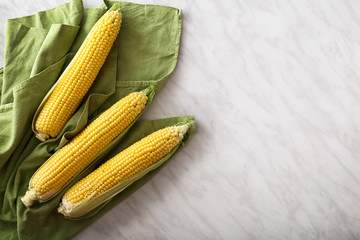Fresh corn on cobs on marble table with green towel. Top view witn copy space.