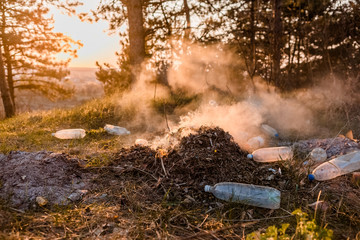 A pile of burning leaves next to a some bottles in the forest.