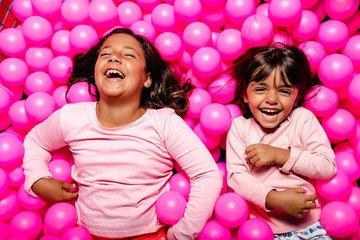 two little girls smiling and playing at pink ball pool