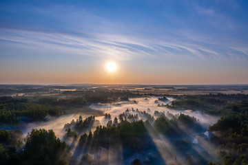 The rays of the morning sun make their way through the thick fog over the forest, field and river