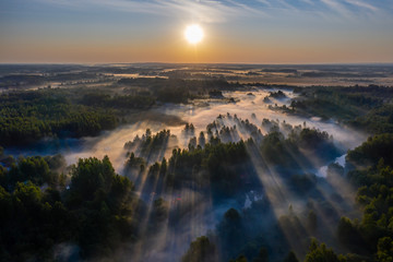 The rays of the morning sun make their way through the thick fog over the forest, field and river