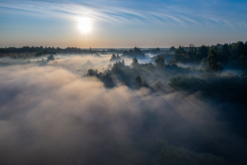 The rays of the morning sun make their way through the thick fog over the forest, field and river