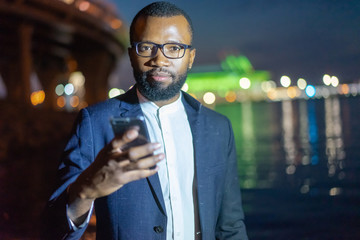 African student walking in the evening city. A man holding a smartphone. A business man answers letters from his smartphone. Business activity.