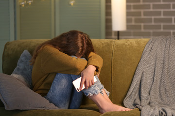 Offended teenage girl with mobile phone on sofa at night