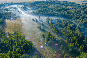 Fog floats over the forest and a field and a star-shaped tent
