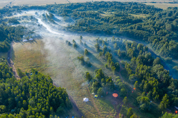 Fog floats over the forest and a field and a star-shaped tent
