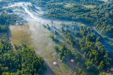 Fog floats over the forest and a field and a star-shaped tent