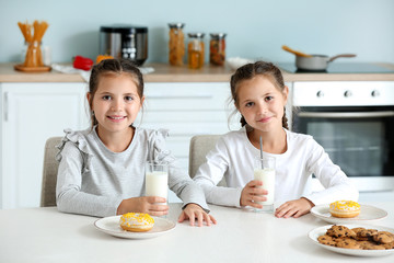 Portrait of cute twin girls drinking milk with sweets in kitchen