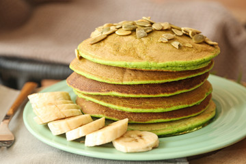 Plate with tasty green pancakes and banana on table