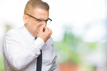 Middle age bussines arab man wearing glasses over isolated background smelling something stinky and disgusting, intolerable smell, holding breath with fingers on nose. Bad smells concept.