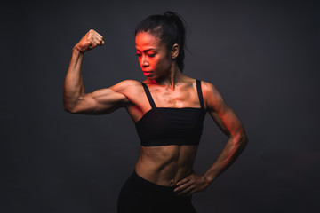 Portrait of healthy athletic 40 year old asian woman with a lean muscle and nice six pack core body lifting her strong right arm and looking toward to her bicep with the warm light and dark background