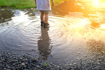 A toddler girl walking through the lake with boots and reflections.