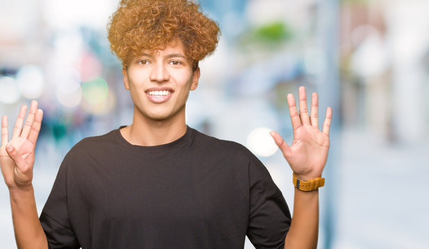 Young handsome man with afro hair wearing black t-shirt showing and pointing up with fingers number nine while smiling confident and happy.