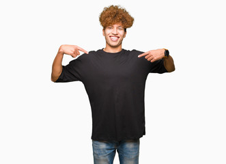 Young handsome man with afro hair wearing black t-shirt looking confident with smile on face,...