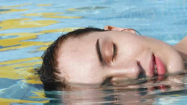 Portrait of a young woman in the water. The girl&rsquo;s face lies halfway in the water. Water treatments for a healthy person. Slow Motion. Close-up.