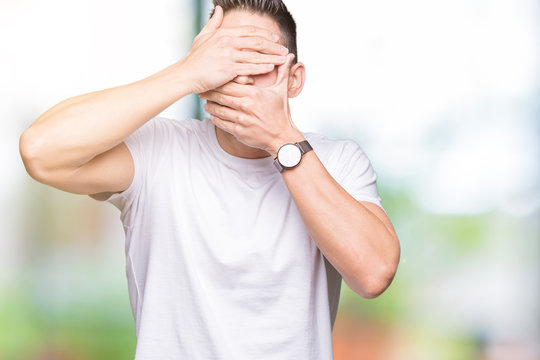 Handsome man wearing white t-shirt over outdoors background Covering eyes and mouth with hands, surprised and shocked. Hiding emotion