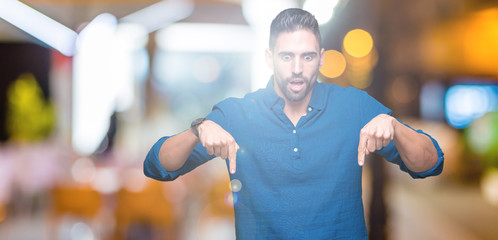 Young handsome man over isolated background Pointing down with fingers showing advertisement, surprised face and open mouth