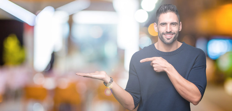 Young handsome man wearing sweater over isolated background amazed and smiling to the camera while presenting with hand and pointing with finger.