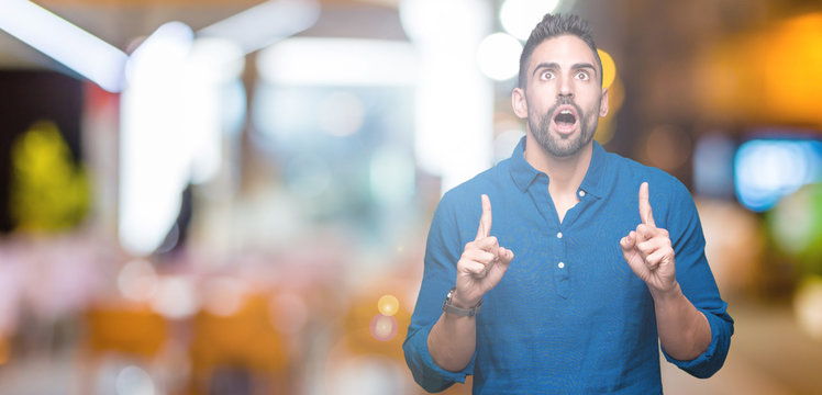 Young handsome man over isolated background amazed and surprised looking up and pointing with fingers and raised arms.