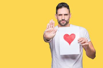 Handsome young man holding card with red heart over isolated background with open hand doing stop sign with serious and confident expression, defense gesture