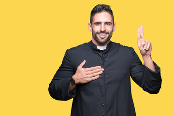 Young Christian priest over isolated background Swearing with hand on chest and fingers, making a...