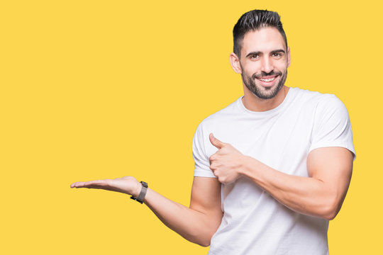 Handsome man wearing white t-shirt over yellow isolated background Showing palm hand and doing ok gesture with thumbs up, smiling happy and cheerful