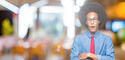 Young african american business man with afro hair wearing glasses and red tie afraid and shocked with surprise expression, fear and excited face.