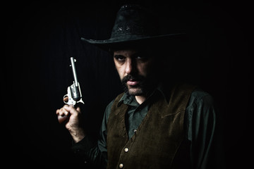 A cowboy holding up a revolver handgun against a dark background.