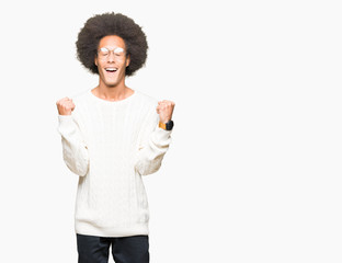 Young african american man with afro hair wearing glasses celebrating surprised and amazed for success with arms raised and open eyes. Winner concept.