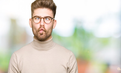 Obraz premium Young handsome business man wearing glasses making fish face with lips, crazy and comical gesture. Funny expression.