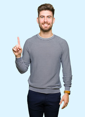 Young handsome man wearing stripes sweater showing and pointing up with finger number one while smiling confident and happy.