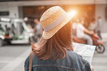 Smiling woman traveler in thapae gate landmark chiangmai thailand with backpack holding world map on holiday, relaxation concept, travel concept