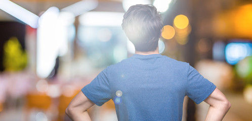 Young handsome man wearing blue t-shirt over isolated background standing backwards looking away with arms on body