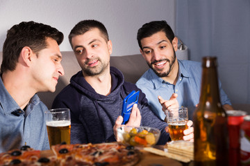 friends looking at phone while drinking beer