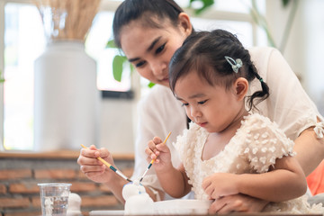 Asian pretty young mother and her daughter paining the plaster doll together. The mom looking the little girl  with happiness. Good relationship of mom and kid. Family activity and education concept.