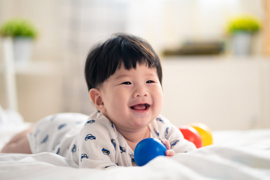 Asian cute baby crawling and playing toy balls on bed at home. Baby is smiling and feeling happy. Choosing the right age of suitable child toy to develop skill of the kid. Mother and baby concept.