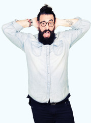 Fototapeta premium Young hipster man with long hair and beard wearing glasses Crazy and scared with hands on head, afraid and surprised of shock with open mouth