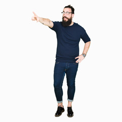 Young hipster man with long hair and beard wearing glasses Pointing with finger surprised ahead, open mouth amazed expression, something in front