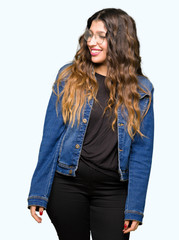 Young beautiful woman wearing glasses and denim jacket looking away to side with smile on face, natural expression. Laughing confident.