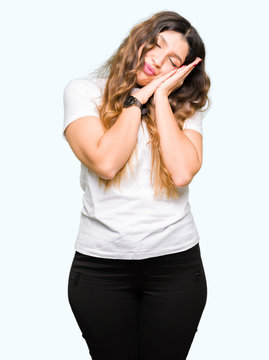 Young beautiful woman wearing casual white t-shirt sleeping tired dreaming and posing with hands together while smiling with closed eyes.
