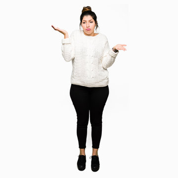 Young beautiful woman wearing winter sweater clueless and confused expression with arms and hands raised. Doubt concept.