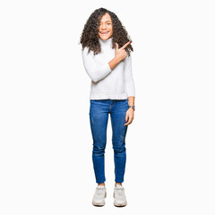 Young beautiful woman with curly hair wearing turtleneck sweater cheerful with a smile of face pointing with hand and finger up to the side with happy and natural expression on face