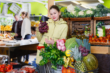 Obraz premium Preteen girl choosing ripe fruits and vegetables in greengrocery