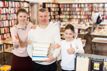 parents and girl standing with stack of books